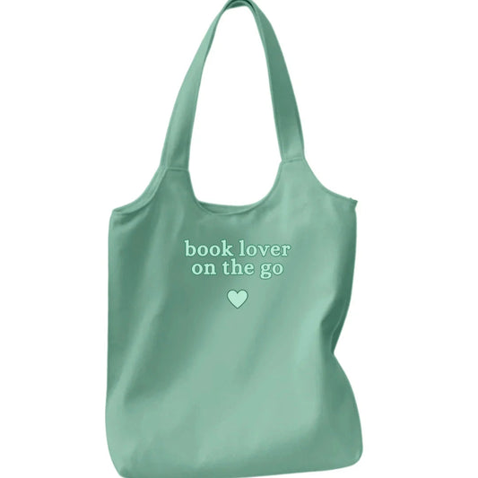 Mint green tote bag with 'book lover on the go' text and heart symbol on a white background
